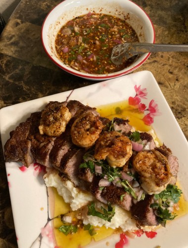 Sliced grilled steak topped with shrimp and cilantro over mashed potatoes, served with Nam Jim Jaew, Thailand's favorite dipping sauce for meats